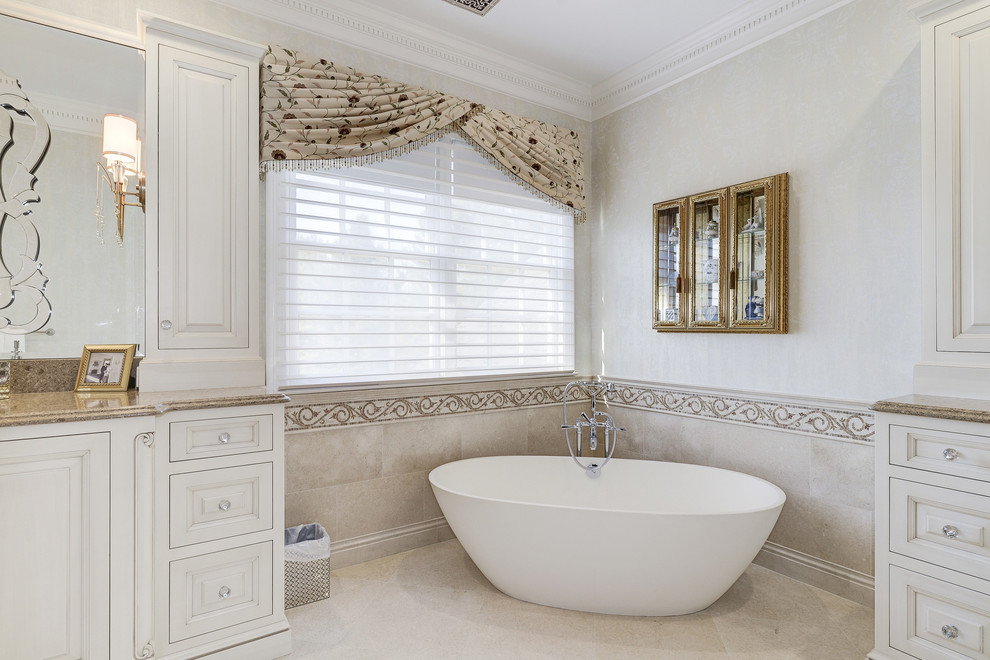 Large transitional master beige tile and stone tile travertine floor freestanding bathtub photo in DC Metro with raised-panel cabinets, beige cabinets, a two-piece toilet, beige walls, an integrated sink and granite countertops