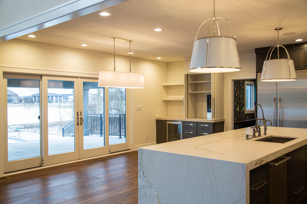 Expansive modern u-shaped kitchen/diner in Indianapolis with a submerged sink, recessed-panel cabinets, grey cabinets, quartz worktops, white splashback, porcelain splashback, stainless steel appliances, laminate floors, an island, brown floors and white worktops.
