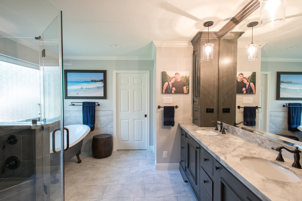 This is an example of a mid-sized transitional master bathroom in Houston with an undermount sink, furniture-like cabinets, brown cabinets, marble benchtops, a freestanding tub, a corner shower, a one-piece toilet, gray tile, stone tile, grey walls and marble floors.