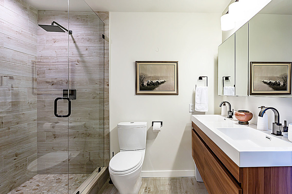 Photo of a mid-sized modern master bathroom in Richmond with flat-panel cabinets, medium wood cabinets, an alcove shower, a two-piece toilet, gray tile, porcelain tile, white walls, porcelain floors, a trough sink, solid surface benchtops, beige floor, a hinged shower door and white benchtops.