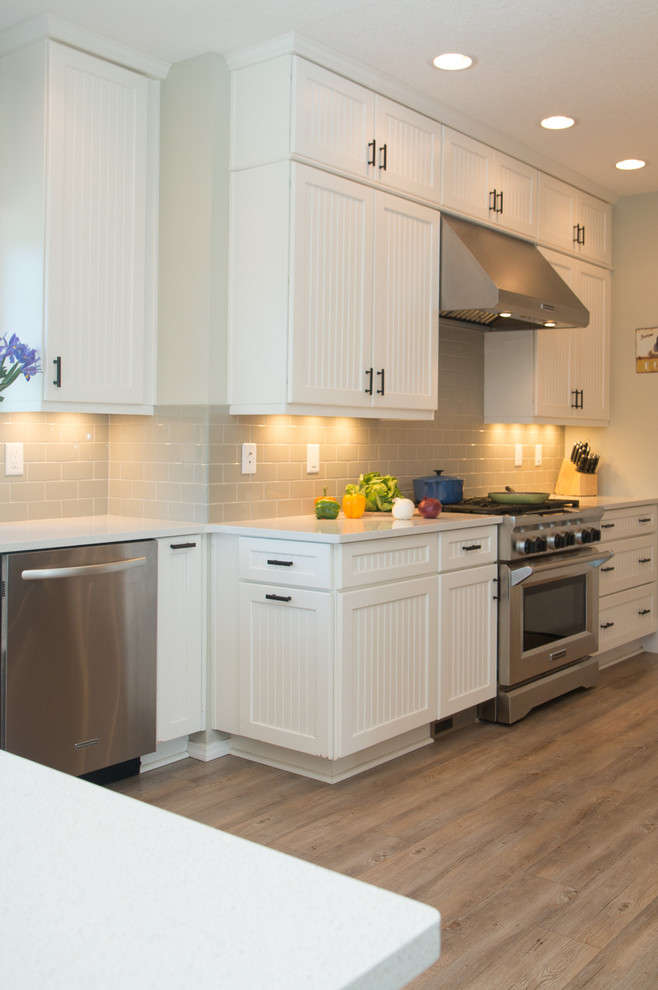 This is an example of a large country u-shaped separate kitchen in Portland with a farmhouse sink, white cabinets, ceramic splashback, stainless steel appliances, vinyl floors, a peninsula, grey splashback, louvered cabinets, quartz benchtops and brown floor.