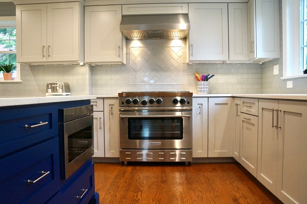 Photo of a mid-sized traditional u-shaped eat-in kitchen in Philadelphia with an undermount sink, shaker cabinets, blue cabinets, quartz benchtops, blue splashback, ceramic splashback, stainless steel appliances, medium hardwood floors, with island, brown floor and white benchtop.