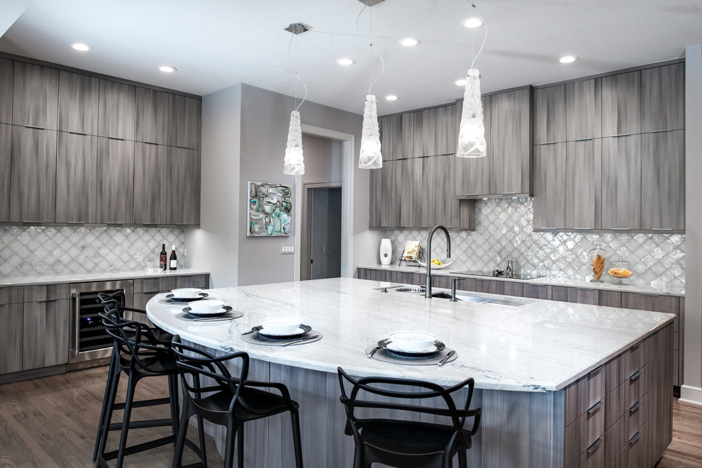 Large transitional medium tone wood floor and brown floor open concept kitchen photo with an undermount sink, flat-panel cabinets, brown cabinets, quartzite countertops, white backsplash, ceramic backsplash, stainless steel appliances, an island and beige countertops