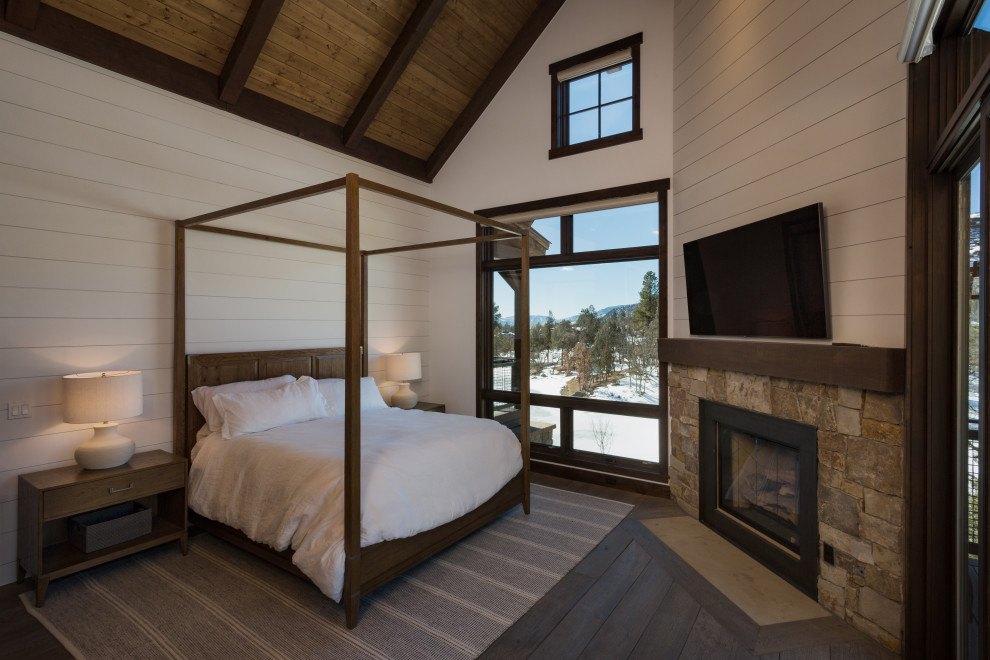 Cette photo montre une chambre montagne en bois de taille moyenne avec un mur blanc, un manteau de cheminée en pierre, un sol gris et poutres apparentes.