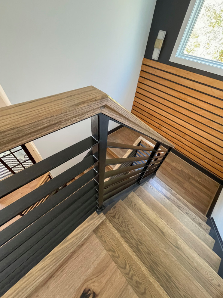 Imagen de escalera recta contemporánea grande con escalones de madera, barandilla de varios materiales y panelado
