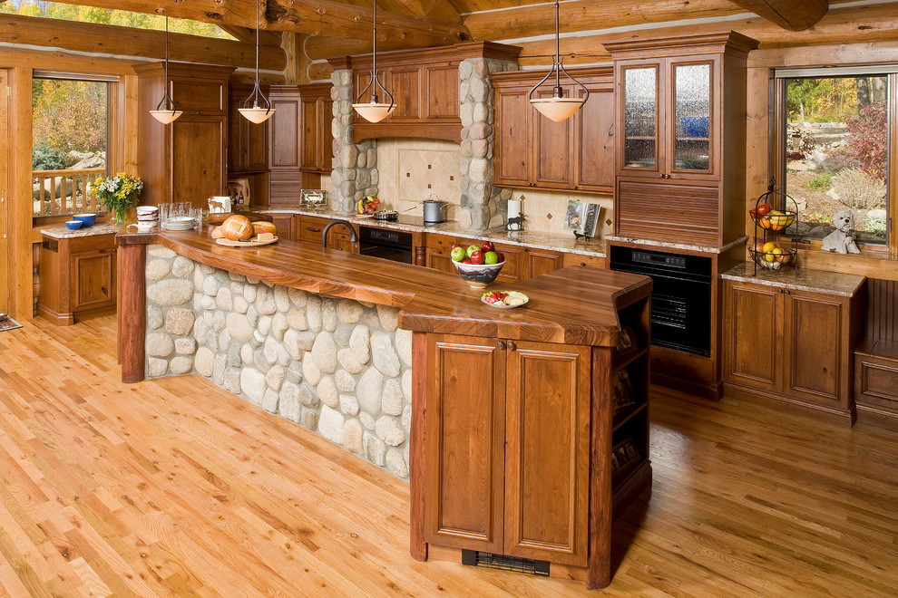 Photo of a country kitchen in Denver with recessed-panel cabinets, dark wood cabinets, wood benchtops, beige splashback, stone tile splashback and black appliances.