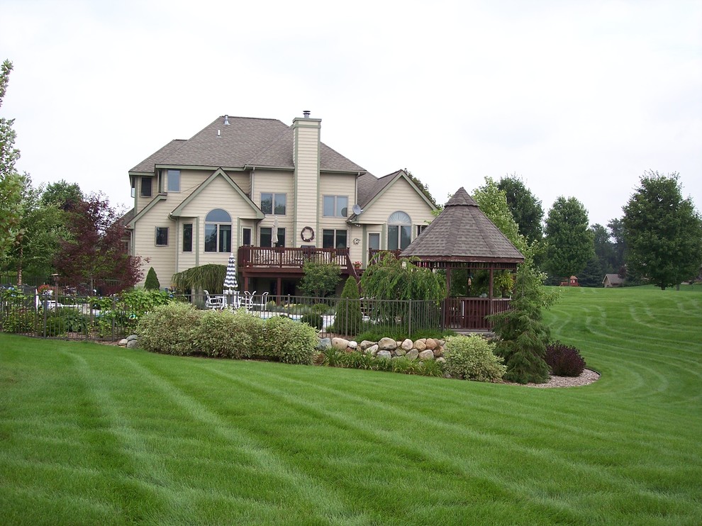 Large arts and crafts side yard custom-shaped natural pool in Grand Rapids with a water feature and concrete slab.