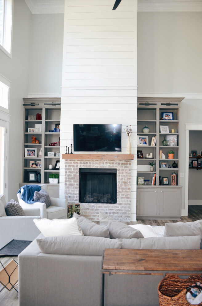 Photo of a country open concept living room in Other with grey walls, light hardwood floors, a standard fireplace, a brick fireplace surround, a wall-mounted tv and beige floor.