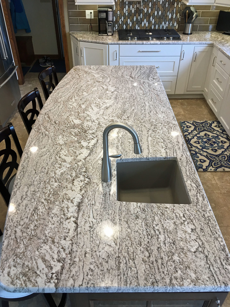 Example of a large transitional l-shaped vinyl floor and beige floor eat-in kitchen design with a double-bowl sink, recessed-panel cabinets, white cabinets, granite countertops, brown backsplash, ceramic backsplash, stainless steel appliances and an island