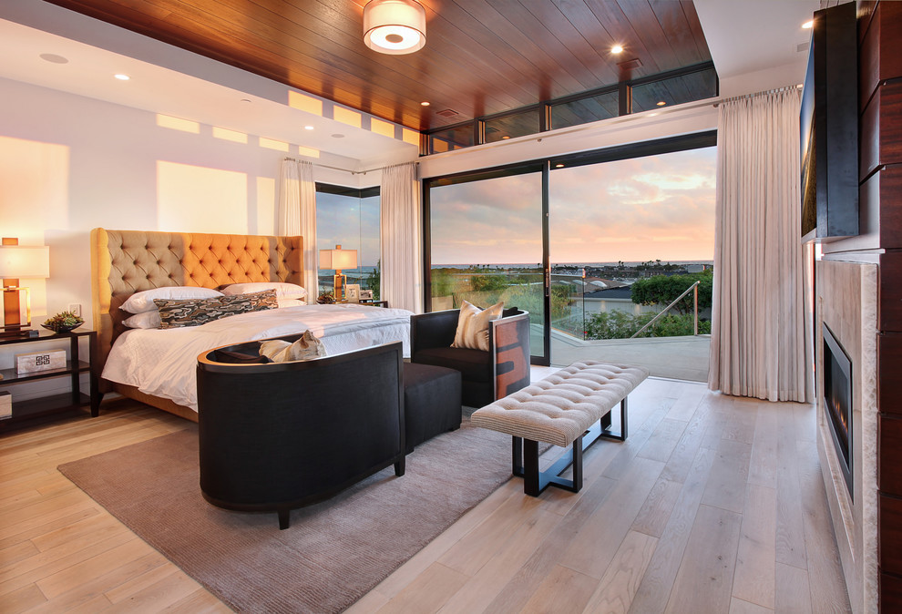 This is an example of a large contemporary master bedroom in Orange County with white walls, light hardwood floors, a stone fireplace surround, a ribbon fireplace and brown floor.