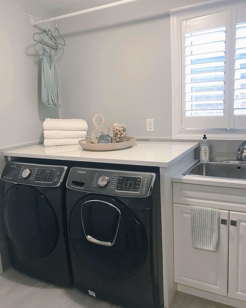 Photo of a small contemporary single-wall laundry room in Toronto with an utility sink, beaded inset cabinets, white cabinets, quartz benchtops, grey walls, ceramic floors, a side-by-side washer and dryer, grey floor and white benchtop.