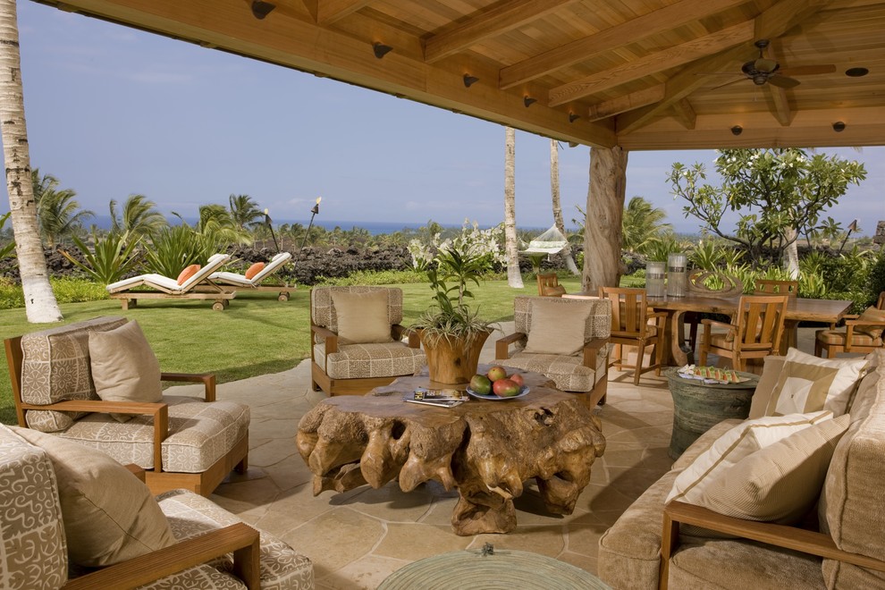 This is an example of a tropical patio in Hawaii with natural stone pavers and a roof extension.
