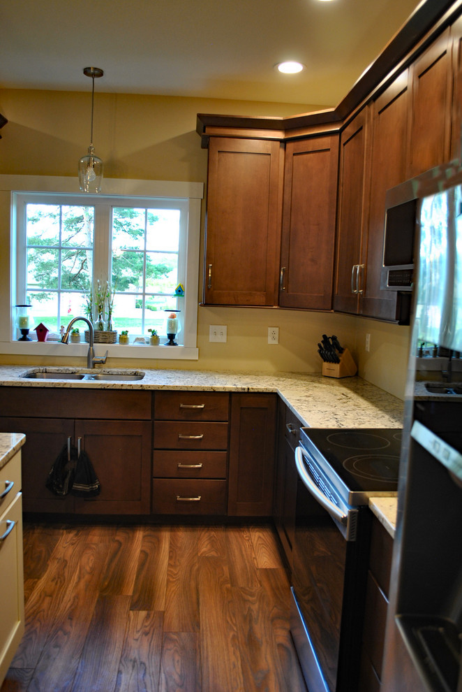 Example of a brown floor kitchen design with brown cabinets, stainless steel appliances, an island and beige countertops