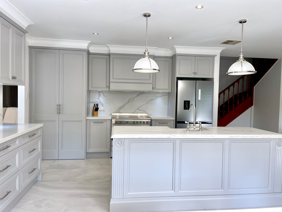 Photo of a large traditional l-shaped eat-in kitchen in Sydney with a farmhouse sink, recessed-panel cabinets, grey cabinets, quartz benchtops, grey splashback, engineered quartz splashback, stainless steel appliances, ceramic floors, with island, grey floor and white benchtop.