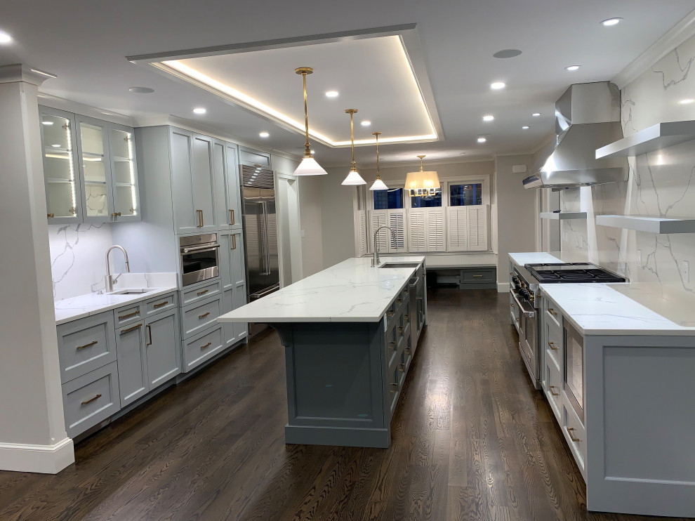 Large transitional galley separate kitchen in Boston with a farmhouse sink, raised-panel cabinets, quartzite benchtops, white splashback, stone slab splashback, stainless steel appliances, dark hardwood floors, with island, brown floor, white benchtop and grey cabinets.