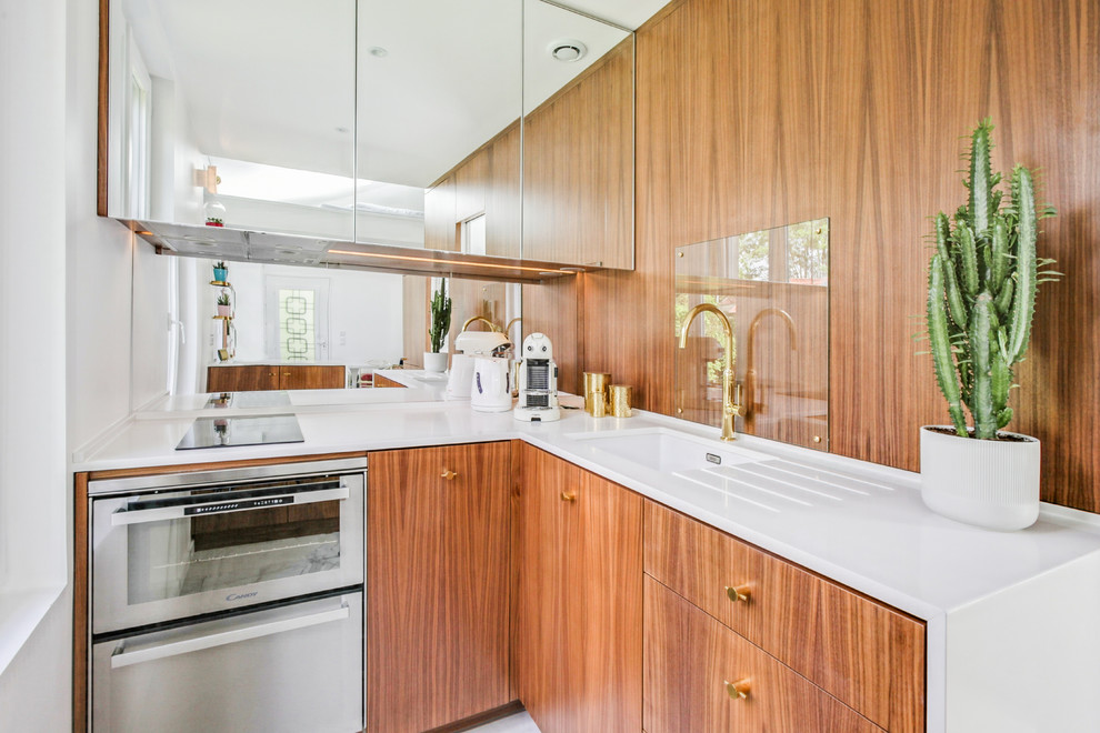 Inspiration pour une cuisine design en L et bois brun avec un évier 1 bac, un placard à porte plane, une crédence miroir, un électroménager en acier inoxydable, aucun îlot et un plan de travail blanc.