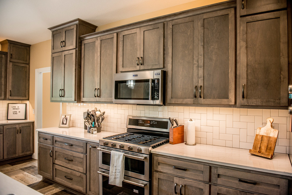 Example of a large transitional l-shaped vinyl floor and multicolored floor open concept kitchen design with a farmhouse sink, shaker cabinets, gray cabinets, quartz countertops, white backsplash, subway tile backsplash, stainless steel appliances, an island and white countertops