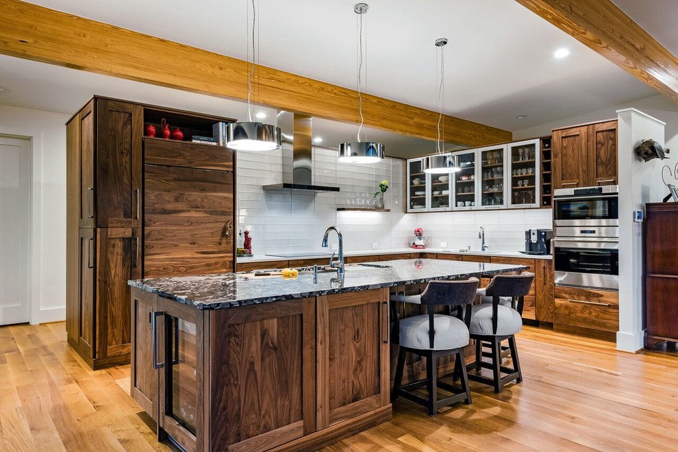 Open concept kitchen - large transitional l-shaped medium tone wood floor and brown floor open concept kitchen idea with an undermount sink, shaker cabinets, dark wood cabinets, granite countertops, white backsplash, glass tile backsplash, stainless steel appliances and an island
