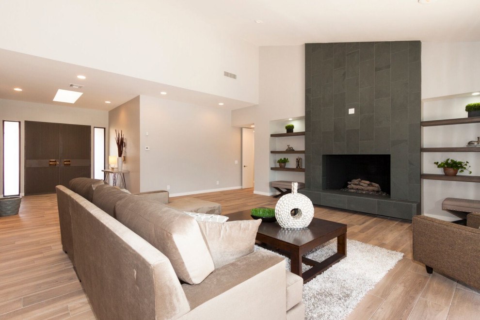 Источник вдохновения для домашнего уюта: большая открытая гостиная комната в стиле ретро с серыми стенами, полом из керамогранита, стандартным камином, фасадом камина из плитки, телевизором на стене и бежевым полом