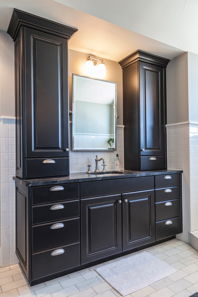 Freestanding bathtub - transitional white tile and subway tile porcelain tile freestanding bathtub idea in Denver with a farmhouse sink, raised-panel cabinets, soapstone countertops, white backsplash, subway tile backsplash, stainless steel appliances, an island, dark wood cabinets, gray walls and an undermount sink