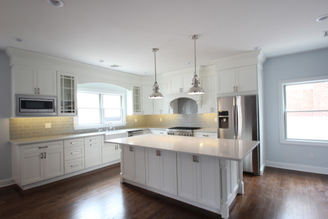 Eat-in kitchen - mid-sized transitional l-shaped brown floor and dark wood floor eat-in kitchen idea with recessed-panel cabinets, white cabinets, quartzite countertops, an island, a farmhouse sink, gray backsplash, ceramic backsplash and stainless steel appliances