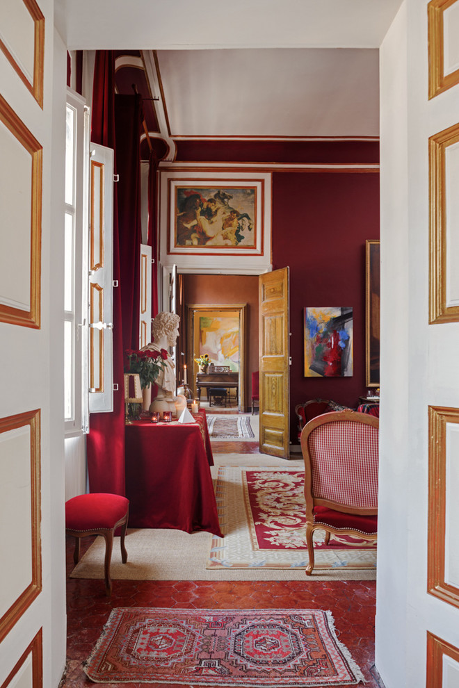 Large transitional hallway in Toulouse with red walls and terra-cotta floors.