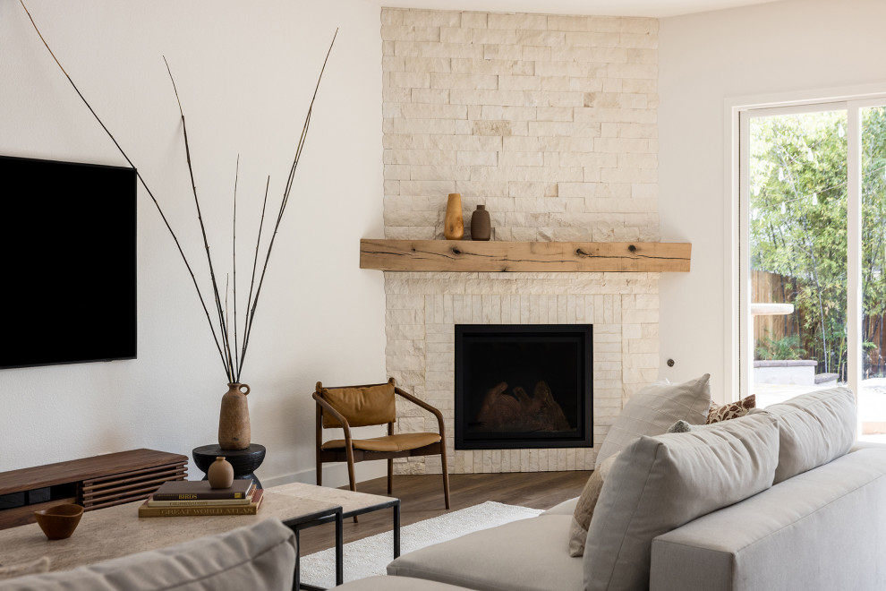 Foto de salón abierto grande con paredes blancas, suelo de madera en tonos medios, chimenea de esquina, marco de chimenea de ladrillo y televisor colgado en la pared
