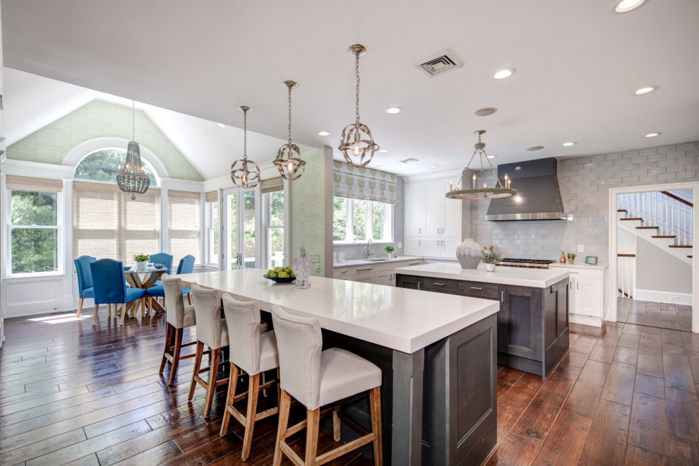 Inspiration for a transitional l-shaped kitchen in Philadelphia with an undermount sink, shaker cabinets, white cabinets, grey splashback, stainless steel appliances, dark hardwood floors, multiple islands, brown floor and white benchtop.