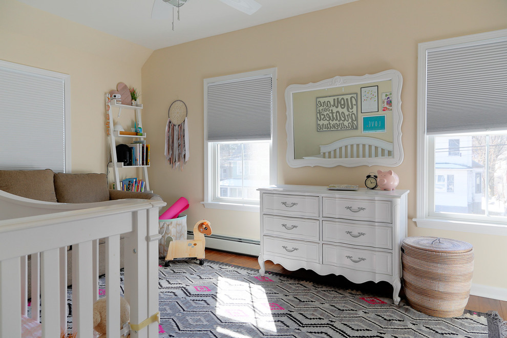 This is an example of a mid-sized traditional nursery for girls in New York with beige walls, medium hardwood floors and brown floor.