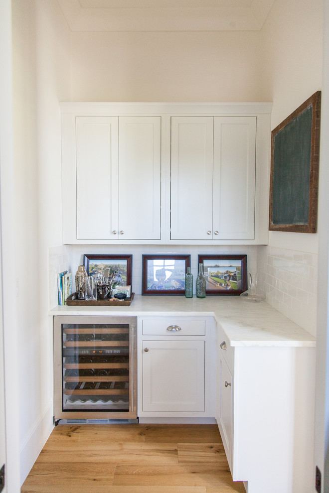 Inspiration for a large transitional l-shaped light wood floor eat-in kitchen remodel in Phoenix with a farmhouse sink, white cabinets, white backsplash, stainless steel appliances, an island, shaker cabinets, stainless steel countertops and porcelain backsplash