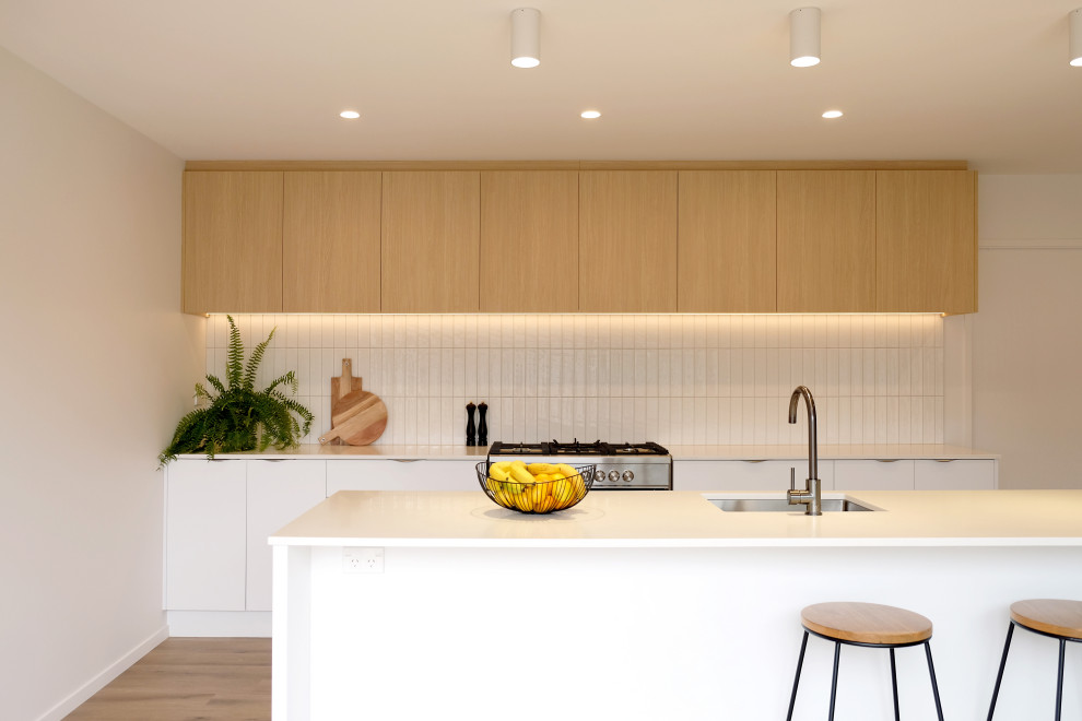 This is an example of a large contemporary kitchen in Other with an undermount sink, flat-panel cabinets, light wood cabinets, solid surface benchtops, white splashback, ceramic splashback, stainless steel appliances, laminate floors, brown floor and white benchtop.