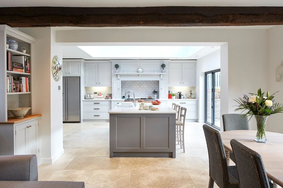 Photo of a large traditional single-wall eat-in kitchen in Wiltshire with a farmhouse sink, recessed-panel cabinets, grey cabinets, quartz benchtops, beige splashback, stone slab splashback, stainless steel appliances, limestone floors and a peninsula.