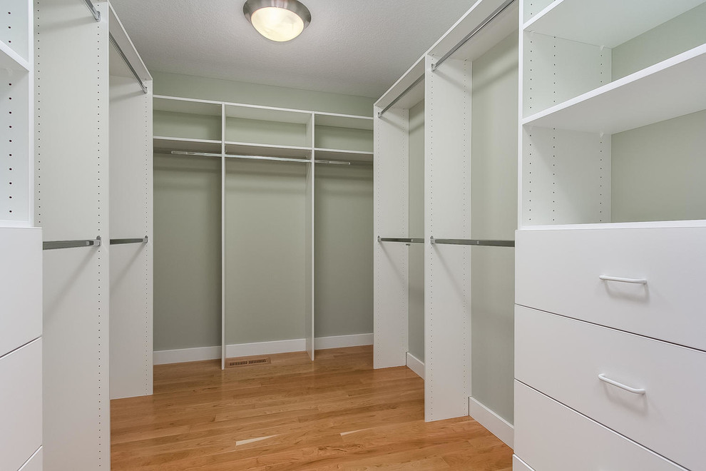 Design ideas for a mid-sized country gender-neutral walk-in wardrobe in Minneapolis with white cabinets, light hardwood floors and open cabinets.