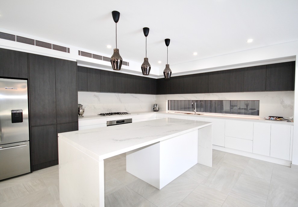 This is an example of an expansive modern l-shaped open plan kitchen in Sydney with a double-bowl sink, flat-panel cabinets, white cabinets, quartz benchtops, white splashback, stone slab splashback, stainless steel appliances, ceramic floors, with island and grey floor.