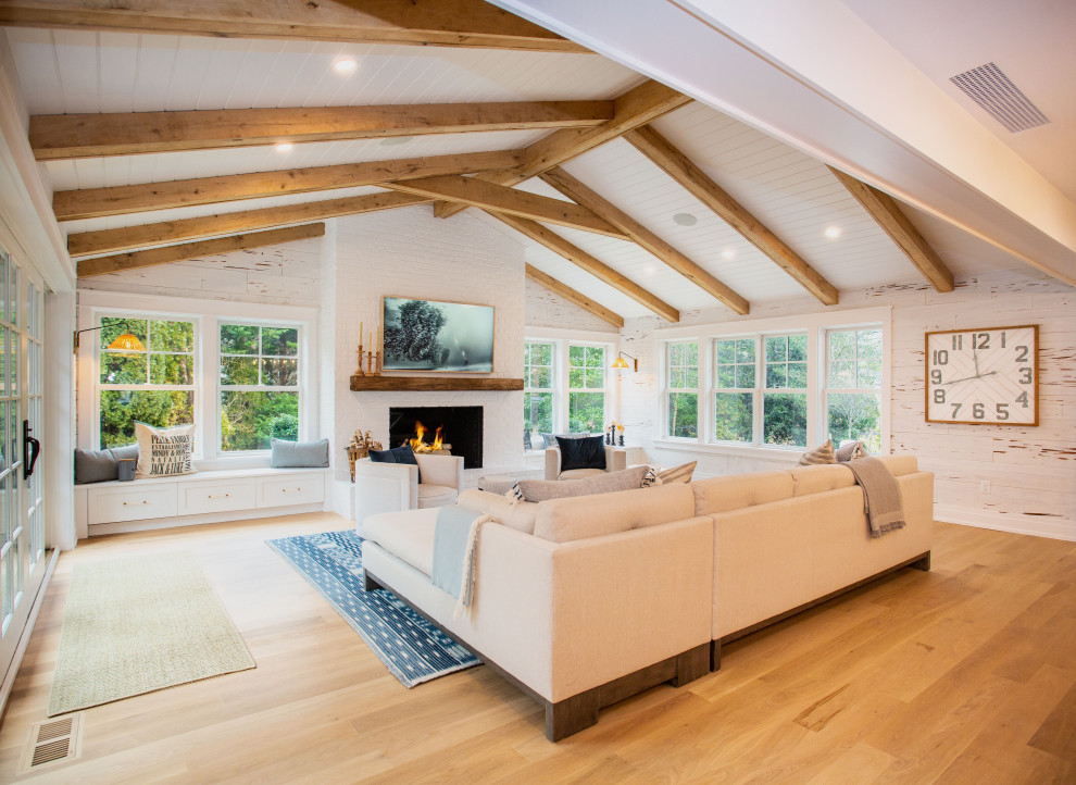 This is an example of a large beach style open concept family room in Other with white walls, medium hardwood floors, a standard fireplace, a brick fireplace surround, a concealed tv, brown floor, exposed beam and planked wall panelling.