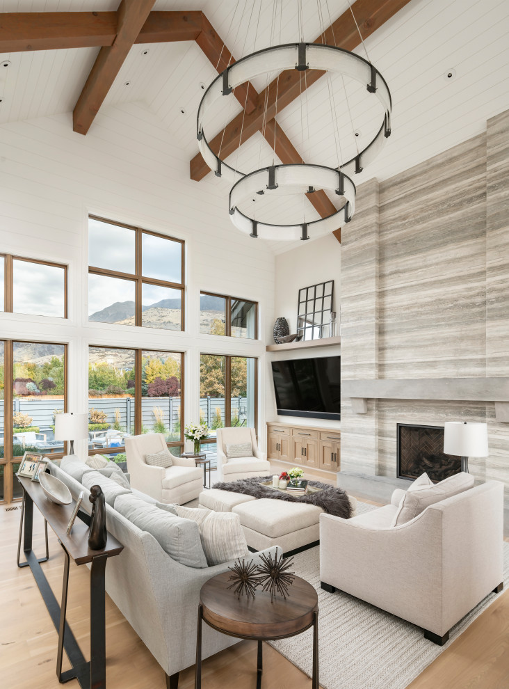 Inspiration for an expansive country open concept living room in Salt Lake City with white walls, light hardwood floors, a standard fireplace, a stone fireplace surround, a wall-mounted tv and beige floor.
