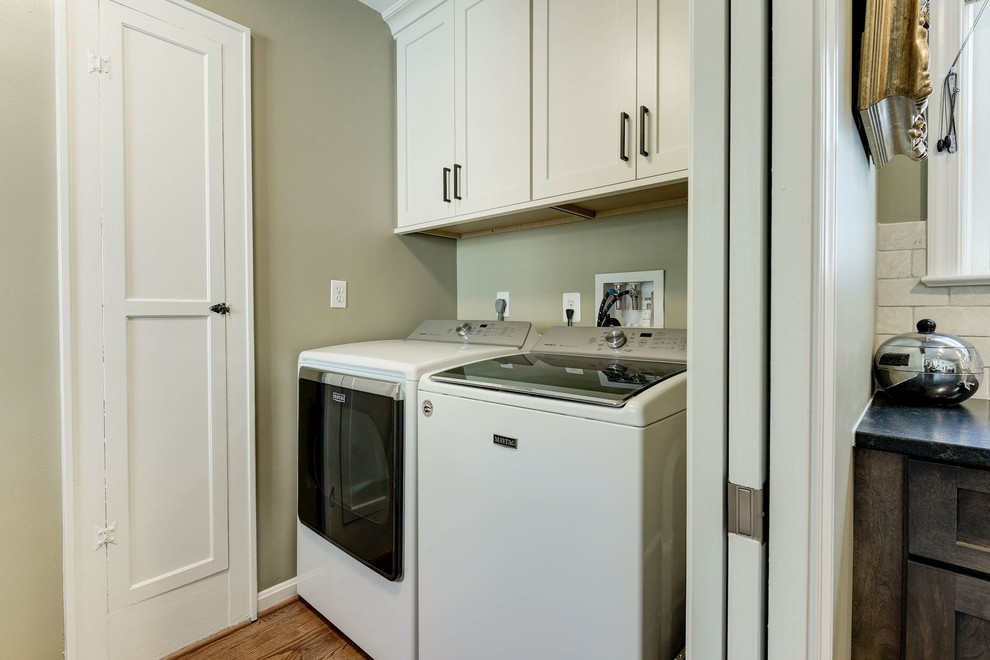 This is an example of a small transitional single-wall laundry cupboard in DC Metro with light hardwood floors, a side-by-side washer and dryer, brown floor, shaker cabinets, white cabinets and grey walls.