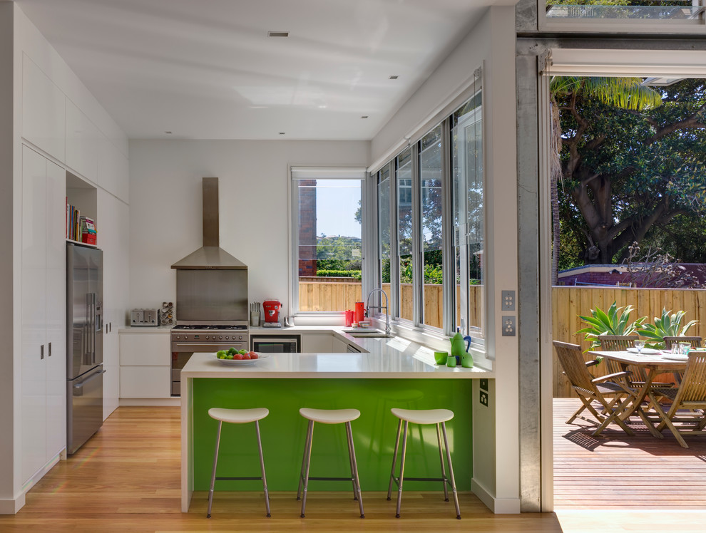 Inspiration for a contemporary u-shaped open plan kitchen in Sydney with a double-bowl sink, flat-panel cabinets, white cabinets, stainless steel appliances, medium hardwood floors and a peninsula.