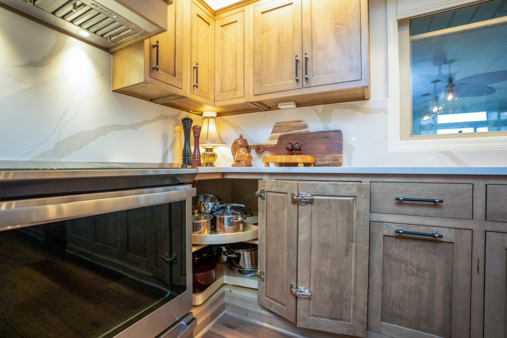 Example of a large transitional l-shaped medium tone wood floor and brown floor eat-in kitchen design with a single-bowl sink, shaker cabinets, medium tone wood cabinets, quartz countertops, white backsplash, quartz backsplash, stainless steel appliances, an island and white countertops