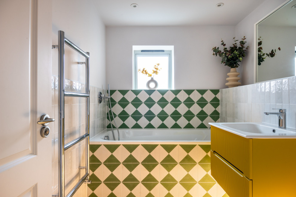 Modernes Badezimmer mit flächenbündigen Schrankfronten, gelben Schränken, Badewanne in Nische, grünen Fliesen, weißen Fliesen, weißer Wandfarbe, Waschtischkonsole, Einzelwaschbecken und schwebendem Waschtisch in Hertfordshire