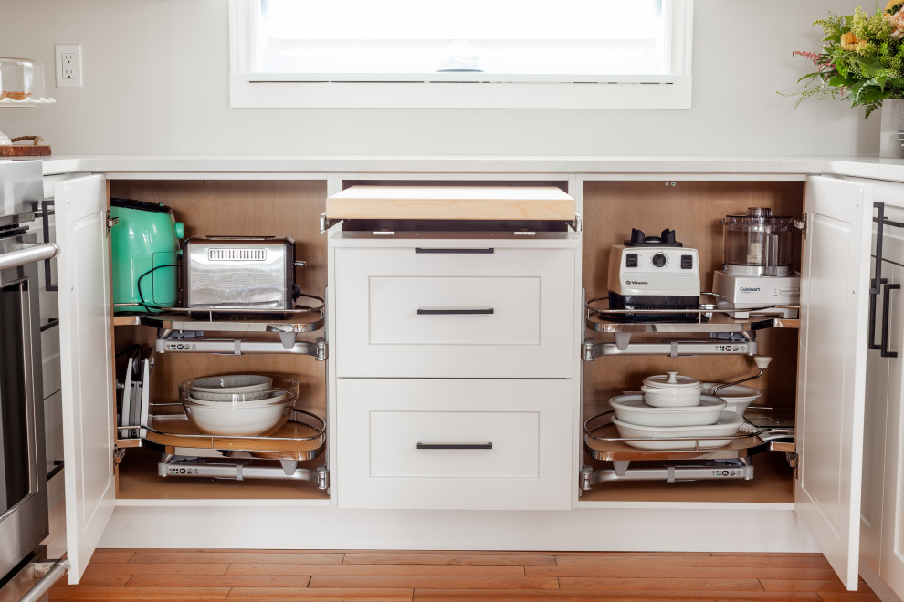 Mid-sized transitional u-shaped light wood floor and brown floor eat-in kitchen photo in Toronto with an undermount sink, shaker cabinets, white cabinets, quartz countertops, white backsplash, stainless steel appliances, no island and white countertops