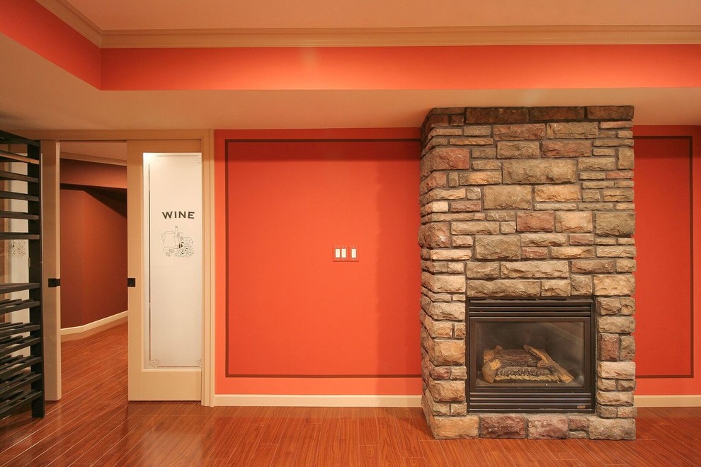 Inspiration for a mid-sized transitional underground medium tone wood floor and brown floor basement remodel in Vancouver with orange walls, a standard fireplace and a stone fireplace