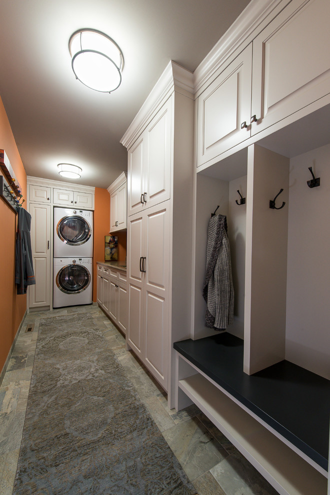 Design ideas for a traditional l-shaped utility room in Minneapolis with raised-panel cabinets, white cabinets, solid surface benchtops, orange walls, porcelain floors and a stacked washer and dryer.
