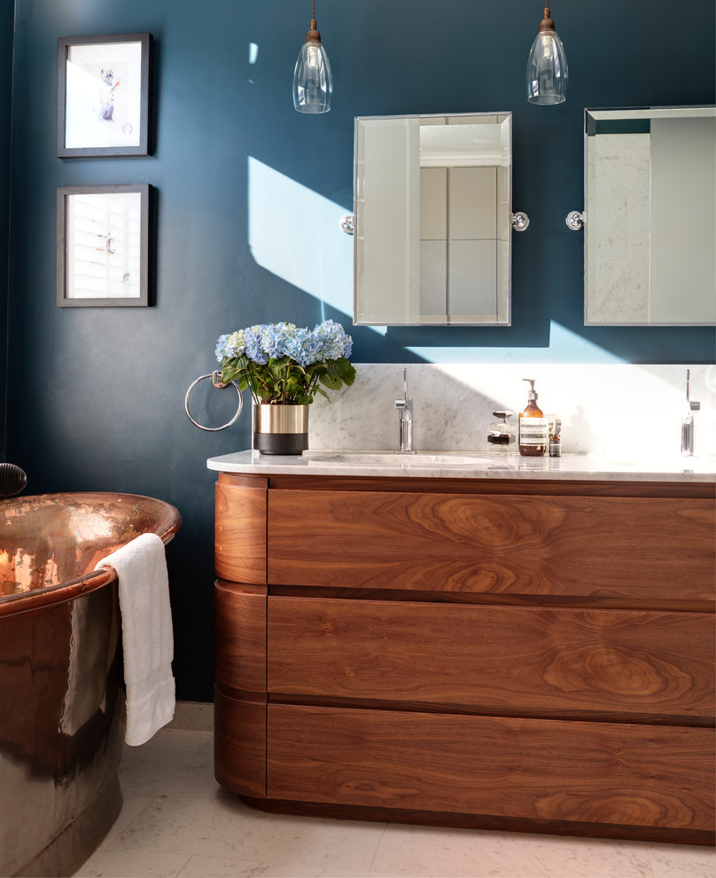 Mid-sized contemporary master bathroom in London with a freestanding tub, blue walls, porcelain floors, marble benchtops, white benchtops, medium wood cabinets, an undermount sink, beige floor and flat-panel cabinets.