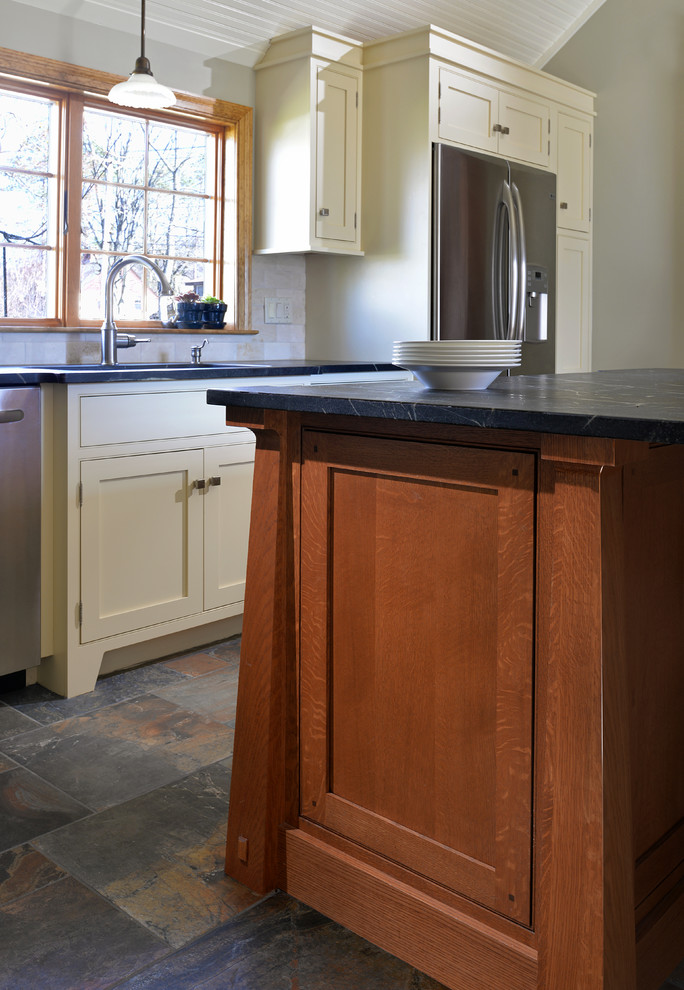 Photo of a mid-sized traditional l-shaped eat-in kitchen in Boston with an undermount sink, beaded inset cabinets, medium wood cabinets, soapstone benchtops, beige splashback, subway tile splashback, stainless steel appliances, slate floors and with island.