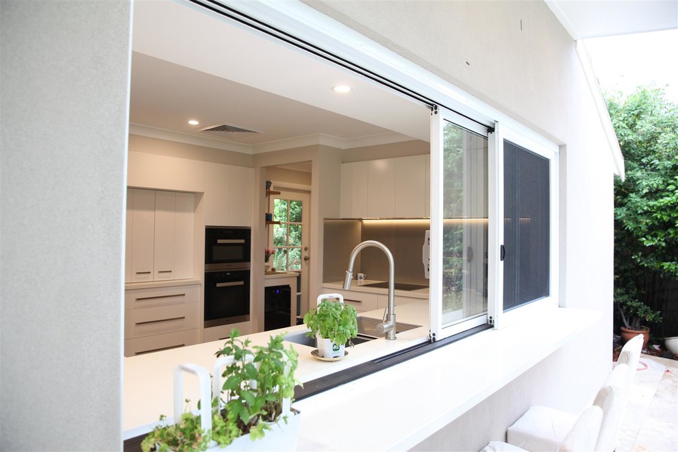 Large contemporary backyard patio in Sydney with an outdoor kitchen, natural stone pavers and a roof extension.