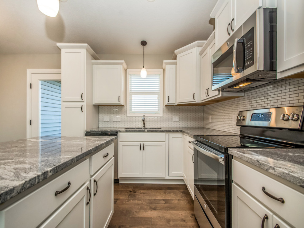 Inspiration for a large transitional medium tone wood floor and brown floor eat-in kitchen remodel with an undermount sink, shaker cabinets, white cabinets, granite countertops, white backsplash, subway tile backsplash, stainless steel appliances, an island and multicolored countertops