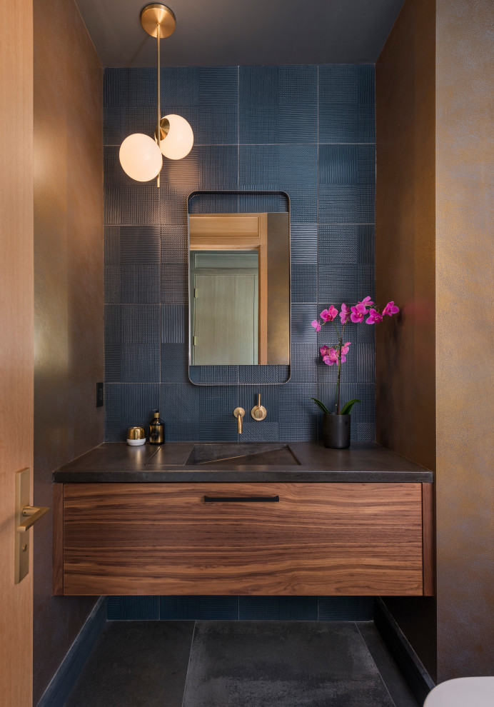 Contemporary powder room in Boston with a floating vanity, flat-panel cabinets, medium wood cabinets, ceramic tile, an integrated sink, grey floor, black benchtops, wallpaper, black tile and brown walls.
