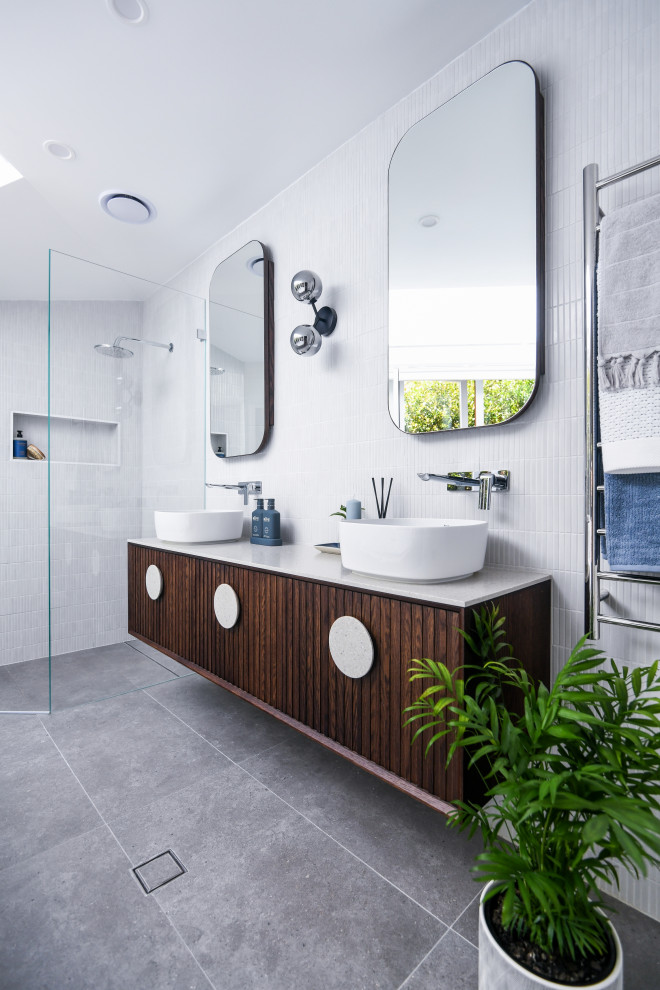 This is an example of a mid-sized contemporary master bathroom in Sydney with furniture-like cabinets, dark wood cabinets, a corner tub, a corner shower, yellow tile, mosaic tile, yellow walls, porcelain floors, a vessel sink, solid surface benchtops, grey floor, a hinged shower door, beige benchtops, a niche, a double vanity and a floating vanity.