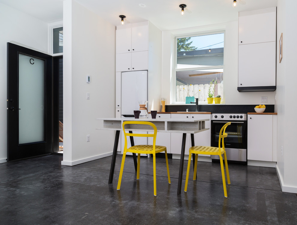 This is an example of a small contemporary single-wall open plan kitchen in Seattle with a single-bowl sink, flat-panel cabinets, white cabinets, wood benchtops, black splashback, white appliances, plywood floors, no island, white floor and brown benchtop.